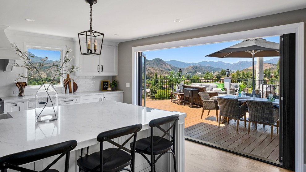 Large transitional single-wall medium tone wood floor and brown floor eat-in kitchen photo with a single-bowl sink, raised-panel cabinets, white cabinets, quartzite countertops, white backsplash, ceramic backsplash, stainless steel appliances, an island and white countertops