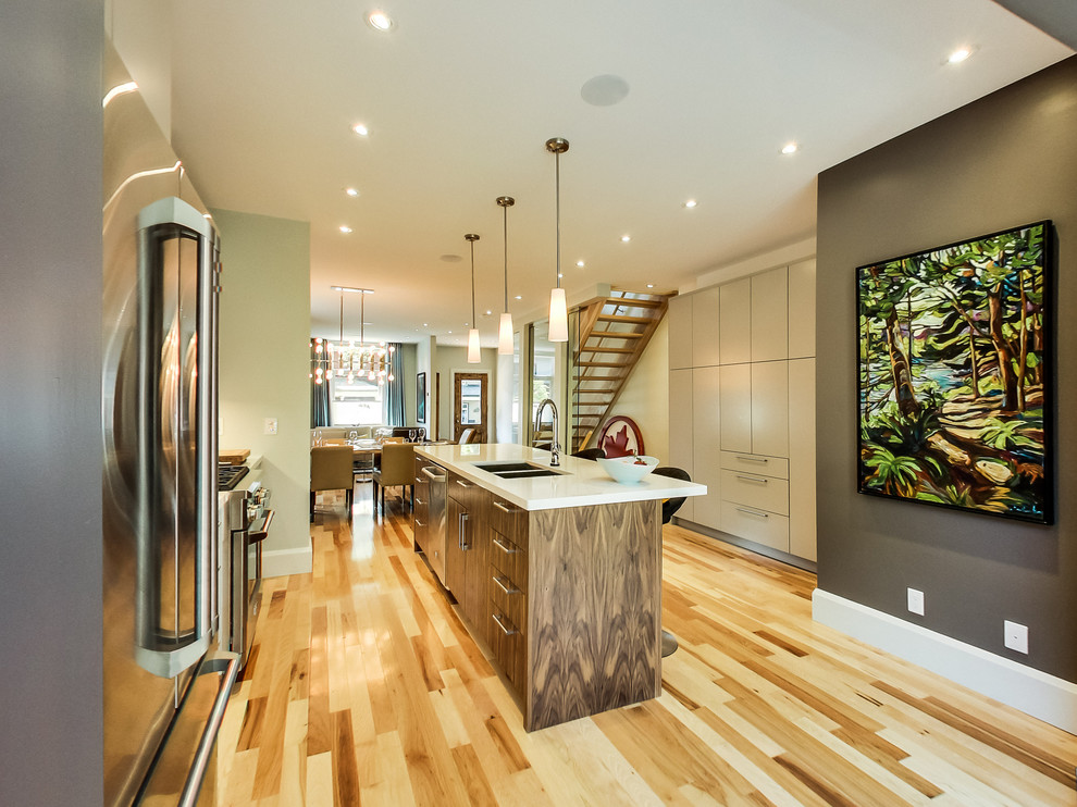 Mid-sized transitional galley light wood floor and multicolored floor kitchen photo in Toronto with a double-bowl sink, flat-panel cabinets, beige cabinets, quartz countertops, gray backsplash, ceramic backsplash, stainless steel appliances and an island