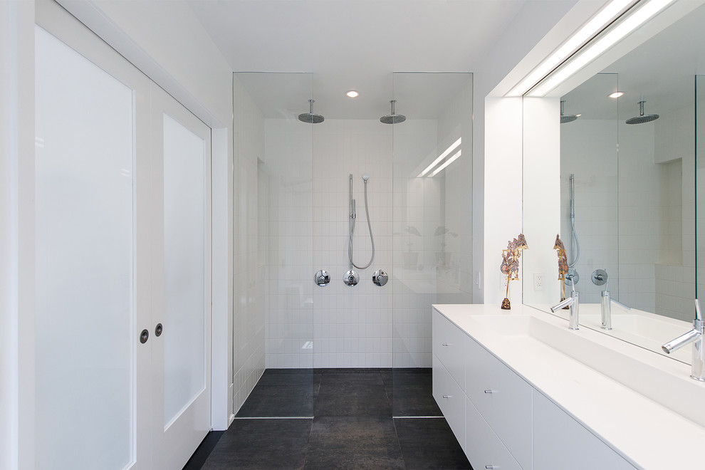 This is an example of a large modern master bathroom in DC Metro with flat-panel cabinets, white cabinets, white walls, porcelain floors, a trough sink, solid surface benchtops, black floor, an open shower, a double shower and white tile.