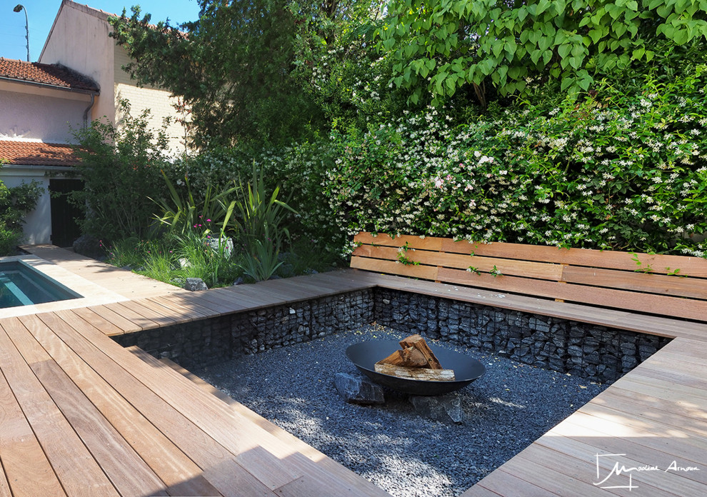 This is an example of a large contemporary full sun garden in Paris with a fire feature and decking.