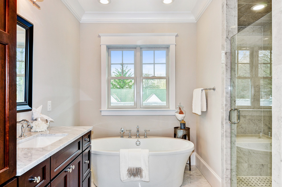 Mid-sized transitional master marble floor and gray floor freestanding bathtub photo in DC Metro with shaker cabinets, dark wood cabinets, beige walls, an undermount sink and a hinged shower door