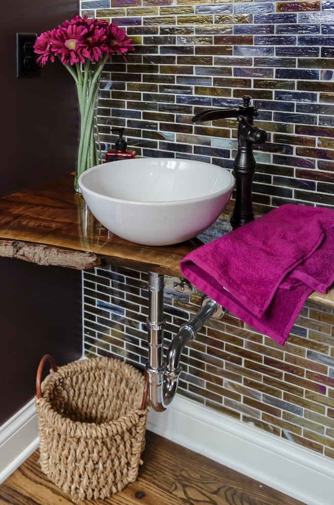 This is an example of a small traditional powder room in Minneapolis with a vessel sink, wood benchtops, multi-coloured tile, glass tile, medium hardwood floors, multi-coloured walls and brown benchtops.