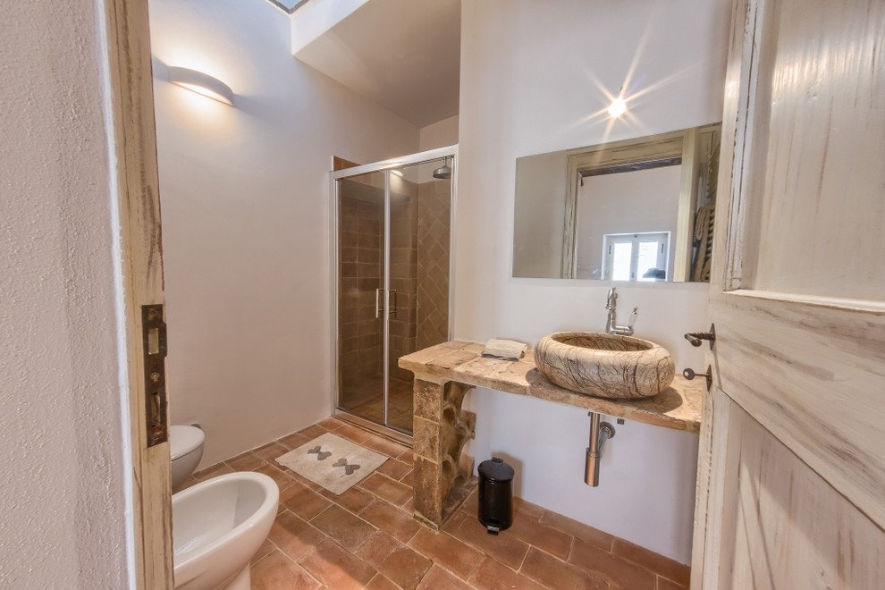 Mid-sized mediterranean 3/4 bathroom in Other with a curbless shower, a wall-mount toilet, terra-cotta tile, terra-cotta floors and a vessel sink.
