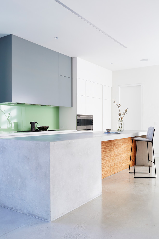 Photo of a mid-sized modern eat-in kitchen in Melbourne with flat-panel cabinets, concrete floors, with island, grey cabinets, green splashback, a double-bowl sink, glass sheet splashback and stainless steel appliances.