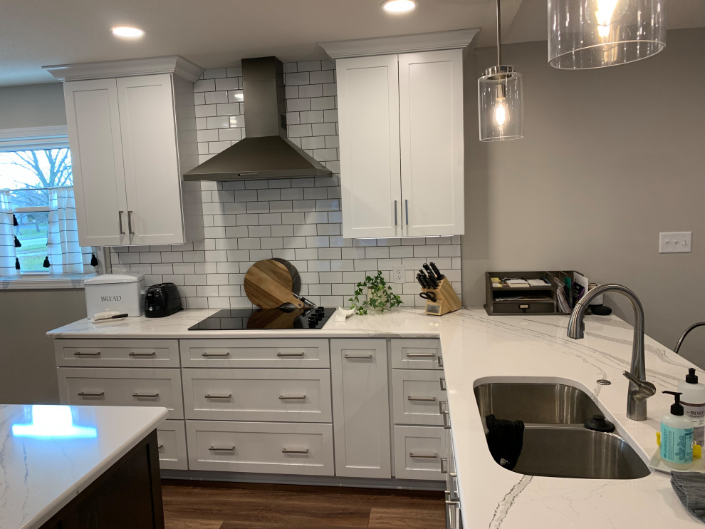 Open concept kitchen - large transitional u-shaped vinyl floor and brown floor open concept kitchen idea with an undermount sink, shaker cabinets, white cabinets, quartz countertops, white backsplash, ceramic backsplash, stainless steel appliances, an island and white countertops