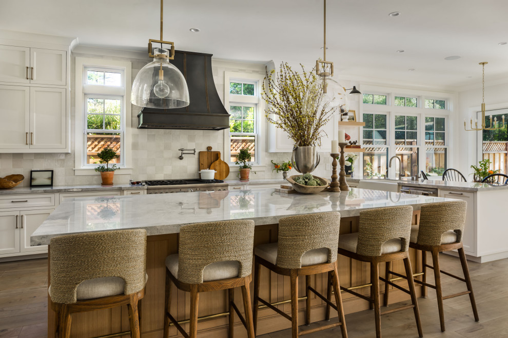 Expansive transitional u-shaped open plan kitchen in San Francisco with a farmhouse sink, shaker cabinets, white cabinets, quartzite benchtops, white splashback, ceramic splashback, stainless steel appliances, medium hardwood floors, with island, grey floor and grey benchtop.