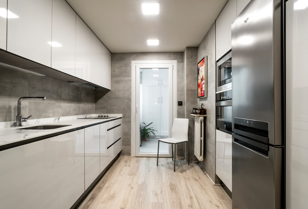 Design ideas for a mid-sized contemporary galley separate kitchen in Other with an undermount sink, flat-panel cabinets, white cabinets, grey splashback, stainless steel appliances, no island, beige floor and light hardwood floors.