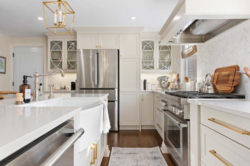 This is an example of a large transitional l-shaped kitchen in Ottawa with a farmhouse sink, shaker cabinets, white cabinets, quartzite benchtops, white splashback, marble splashback, stainless steel appliances, medium hardwood floors, with island and white benchtop.