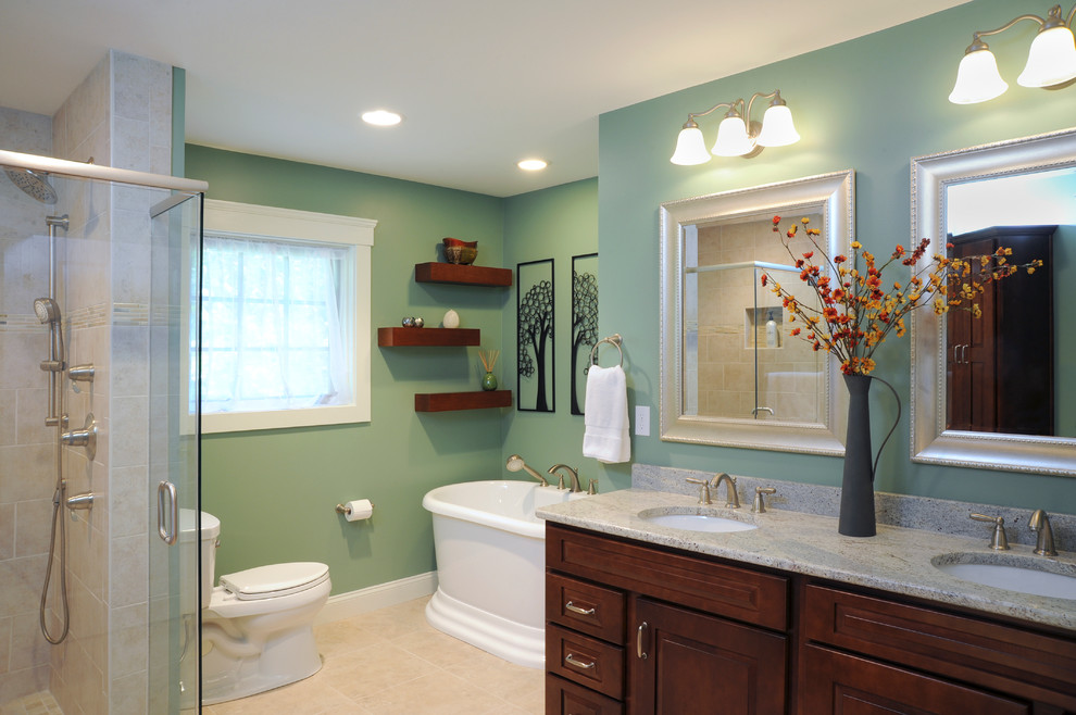 This is an example of a large transitional master bathroom in Cincinnati with an undermount sink, a freestanding tub, a corner shower, green walls, raised-panel cabinets, dark wood cabinets, a two-piece toilet, stone tile, travertine floors and limestone benchtops.