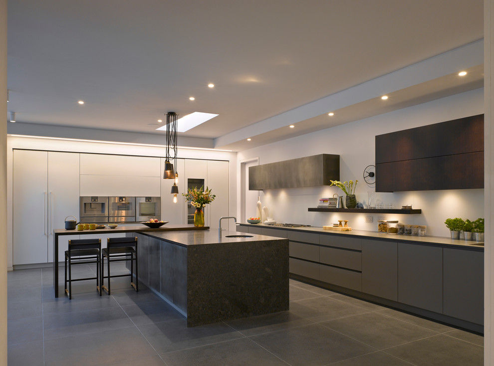 Large contemporary kitchen in London with an undermount sink, flat-panel cabinets, grey cabinets, solid surface benchtops, stainless steel appliances, with island and grey floor.