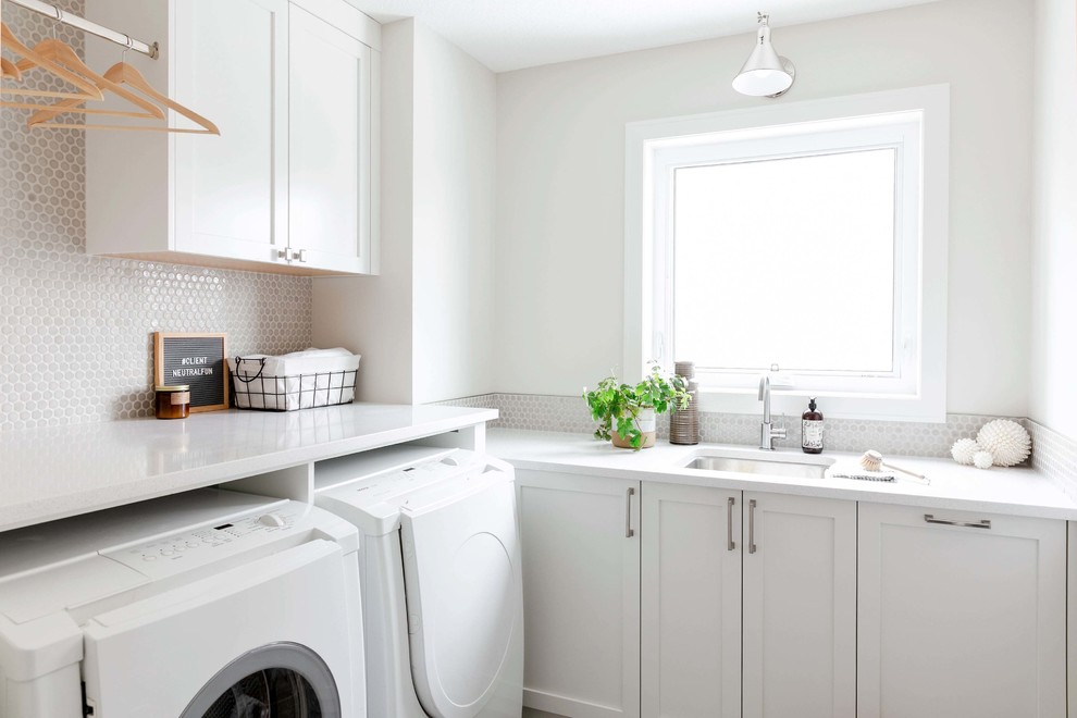 Inspiration for a mid-sized transitional l-shaped utility room in Calgary with an undermount sink, shaker cabinets, white cabinets, quartzite benchtops, white walls, porcelain floors, a side-by-side washer and dryer, grey floor and white benchtop.