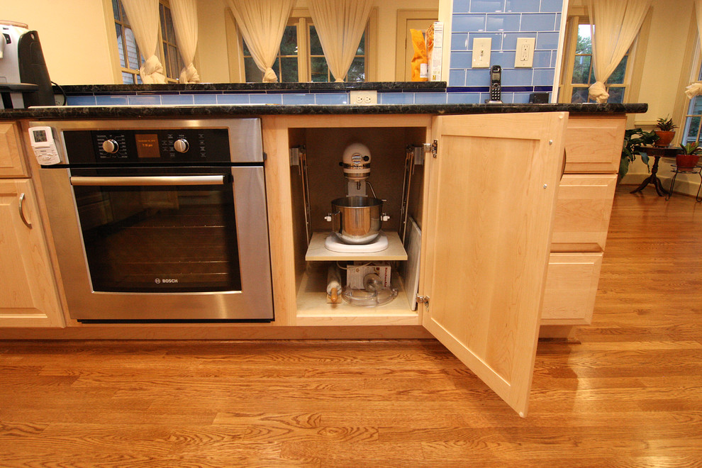 Example of a huge transitional l-shaped medium tone wood floor home design design with an undermount sink, raised-panel cabinets, light wood cabinets, granite countertops, blue backsplash, glass tile backsplash and stainless steel appliances