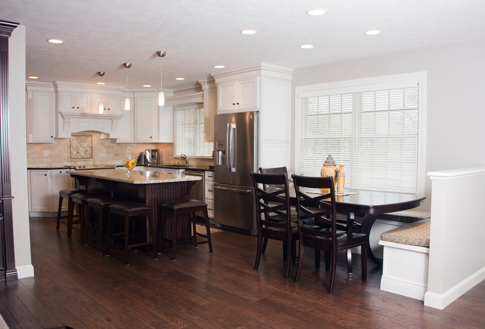 Example of a large transitional u-shaped medium tone wood floor kitchen design in Cincinnati with an undermount sink, recessed-panel cabinets, white cabinets, granite countertops, beige backsplash, stone tile backsplash, stainless steel appliances and an island