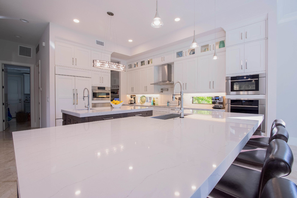 Example of a huge transitional l-shaped porcelain tile and beige floor open concept kitchen design with a farmhouse sink, shaker cabinets, white cabinets, quartz countertops, white backsplash, porcelain backsplash, stainless steel appliances and two islands