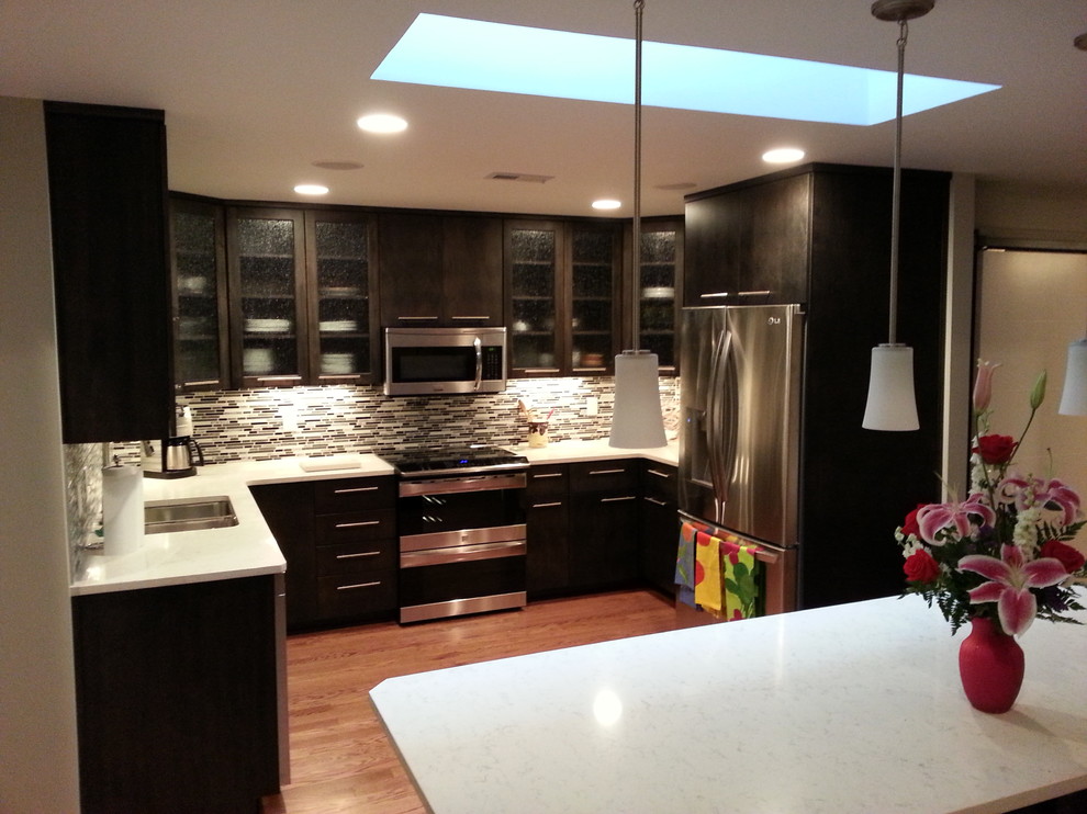 Example of a mid-sized transitional u-shaped medium tone wood floor and brown floor eat-in kitchen design with a double-bowl sink, glass-front cabinets, dark wood cabinets, quartzite countertops, multicolored backsplash, matchstick tile backsplash, stainless steel appliances and an island