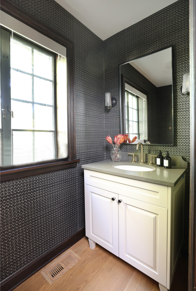 Inspiration for a small traditional powder room in Chicago with recessed-panel cabinets, white cabinets, black walls, light hardwood floors, an undermount sink, engineered quartz benchtops, grey benchtops, a freestanding vanity and wallpaper.