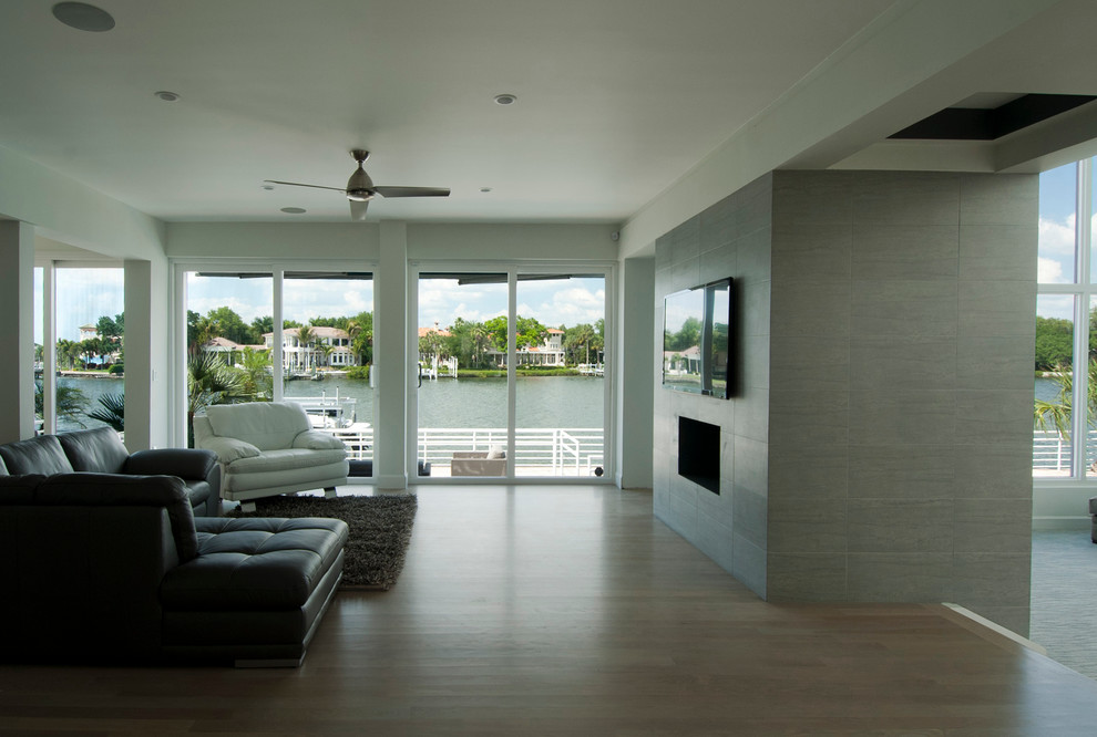 This is an example of a large contemporary open concept living room in Tampa with white walls, light hardwood floors, a two-sided fireplace, a tile fireplace surround and a wall-mounted tv.