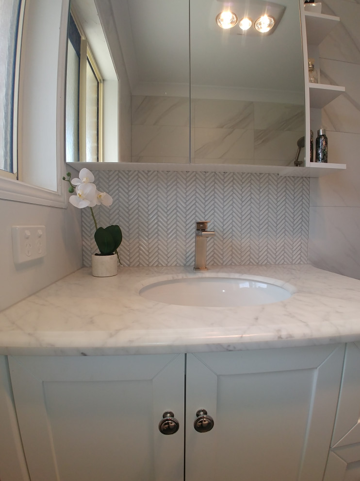 Inspiration for a small transitional master bathroom in Brisbane with shaker cabinets, white cabinets, ceramic tile, porcelain floors, marble benchtops, grey floor, a niche, a single vanity, a freestanding vanity, white tile, a vessel sink, a hinged shower door and white benchtops.