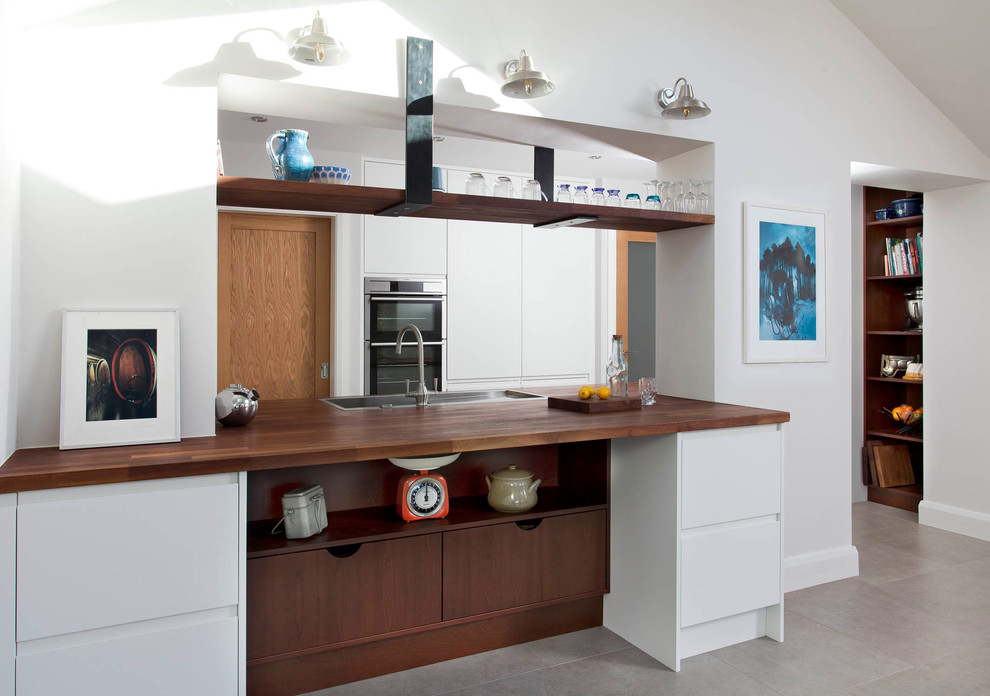 Photo of a mid-sized contemporary u-shaped eat-in kitchen in Other with an undermount sink, flat-panel cabinets, white cabinets, wood benchtops, grey splashback, stone slab splashback, stainless steel appliances, porcelain floors, a peninsula and grey floor.