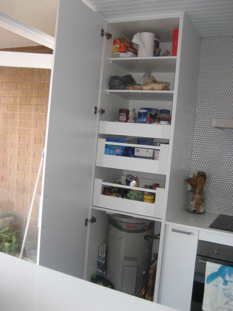 This is an example of a small modern l-shaped kitchen in Sydney with a single-bowl sink, flat-panel cabinets, white cabinets, quartz benchtops, white splashback, stainless steel appliances and with island.