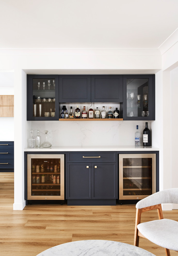 Design ideas for an expansive transitional l-shaped home bar in Sydney with shaker cabinets, blue cabinets, quartz benchtops, white splashback, engineered quartz splashback, laminate floors, brown floor and white benchtop.
