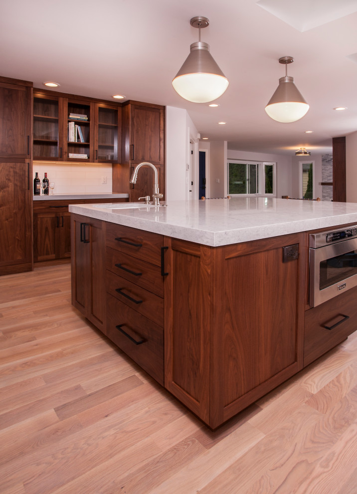 Example of a large transitional u-shaped light wood floor and brown floor eat-in kitchen design in Seattle with a farmhouse sink, dark wood cabinets, white backsplash, subway tile backsplash, stainless steel appliances, an island and white countertops