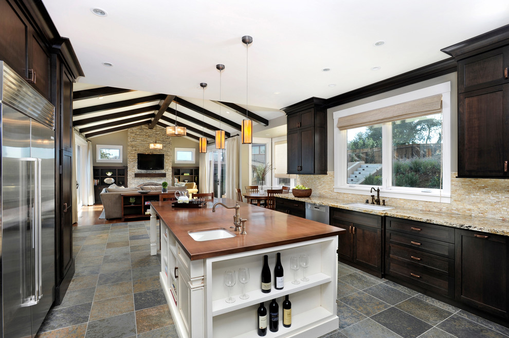 This is an example of a contemporary open plan kitchen in San Francisco with stainless steel appliances, wood benchtops, dark wood cabinets and slate floors.
