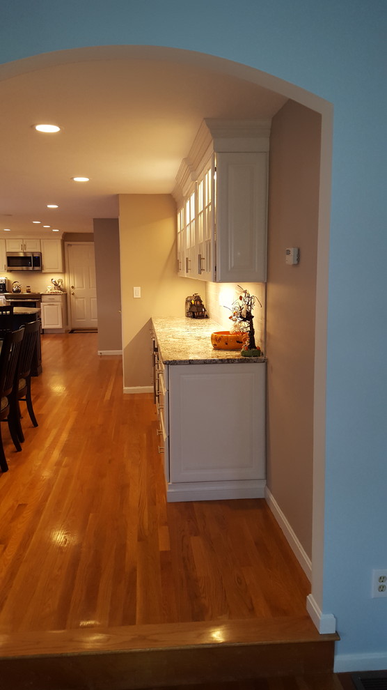Large transitional l-shaped light wood floor eat-in kitchen photo in Boston with an undermount sink, raised-panel cabinets, white cabinets, granite countertops, gray backsplash, ceramic backsplash, stainless steel appliances and an island