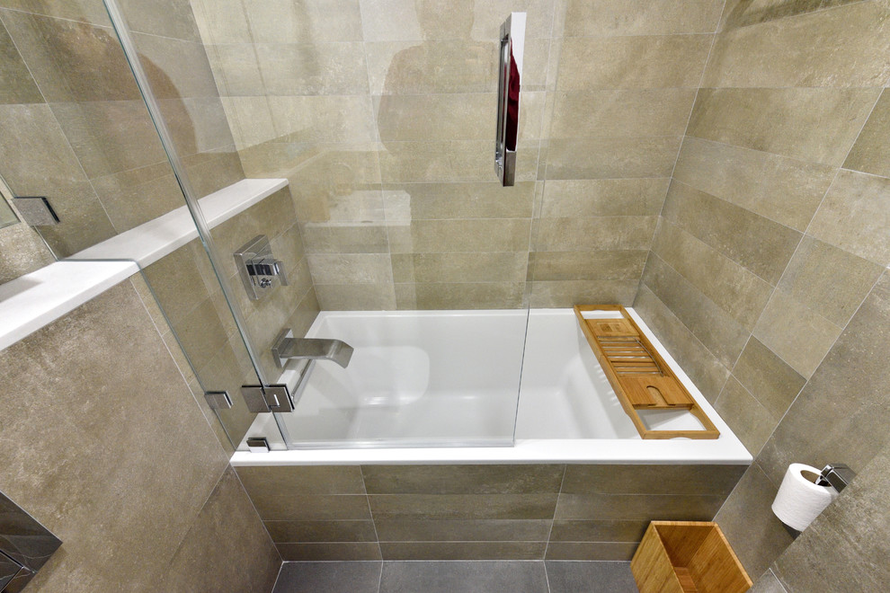 This is an example of a small contemporary master bathroom in New York with flat-panel cabinets, white cabinets, a drop-in tub, a shower/bathtub combo, a wall-mount toilet, gray tile, ceramic tile, multi-coloured walls, ceramic floors and a wall-mount sink.