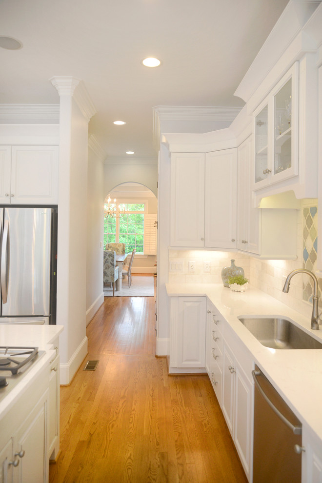 Inspiration for a transitional light wood floor kitchen remodel with white cabinets, beige backsplash, stainless steel appliances and an island