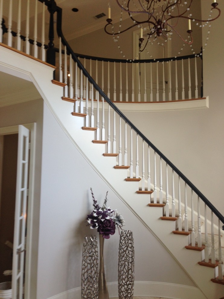 Large traditional wood curved staircase in Atlanta with painted wood risers and wood railing.