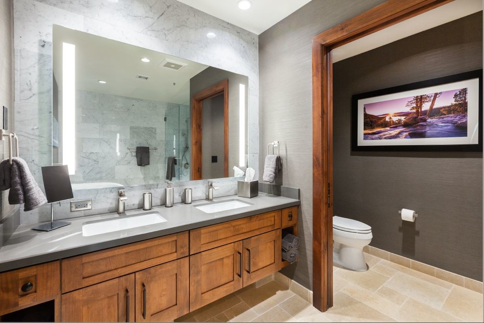 Photo of a large country master bathroom in Other with shaker cabinets, brown cabinets, a freestanding tub, a one-piece toilet, gray tile, marble, grey walls, travertine floors, an undermount sink, concrete benchtops, beige floor and a hinged shower door.