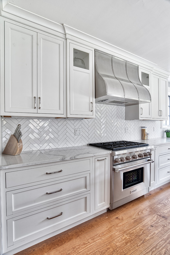 Design ideas for an expansive traditional galley eat-in kitchen in New York with a farmhouse sink, beaded inset cabinets, white cabinets, quartzite benchtops, white splashback, subway tile splashback, stainless steel appliances, medium hardwood floors, with island and white benchtop.