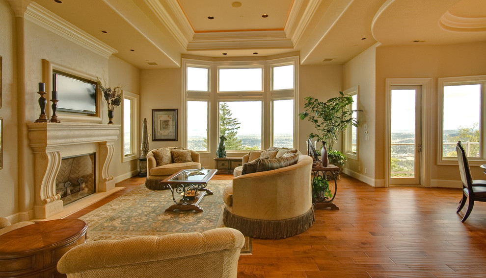 Inspiration for a large transitional formal open concept living room in Portland with beige walls, medium hardwood floors, a standard fireplace, a plaster fireplace surround, a wall-mounted tv and brown floor.