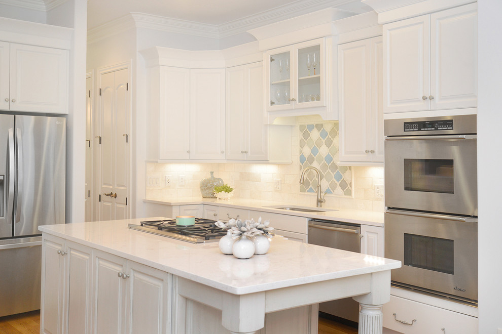 Transitional light wood floor kitchen photo with white cabinets, beige backsplash, stainless steel appliances and an island