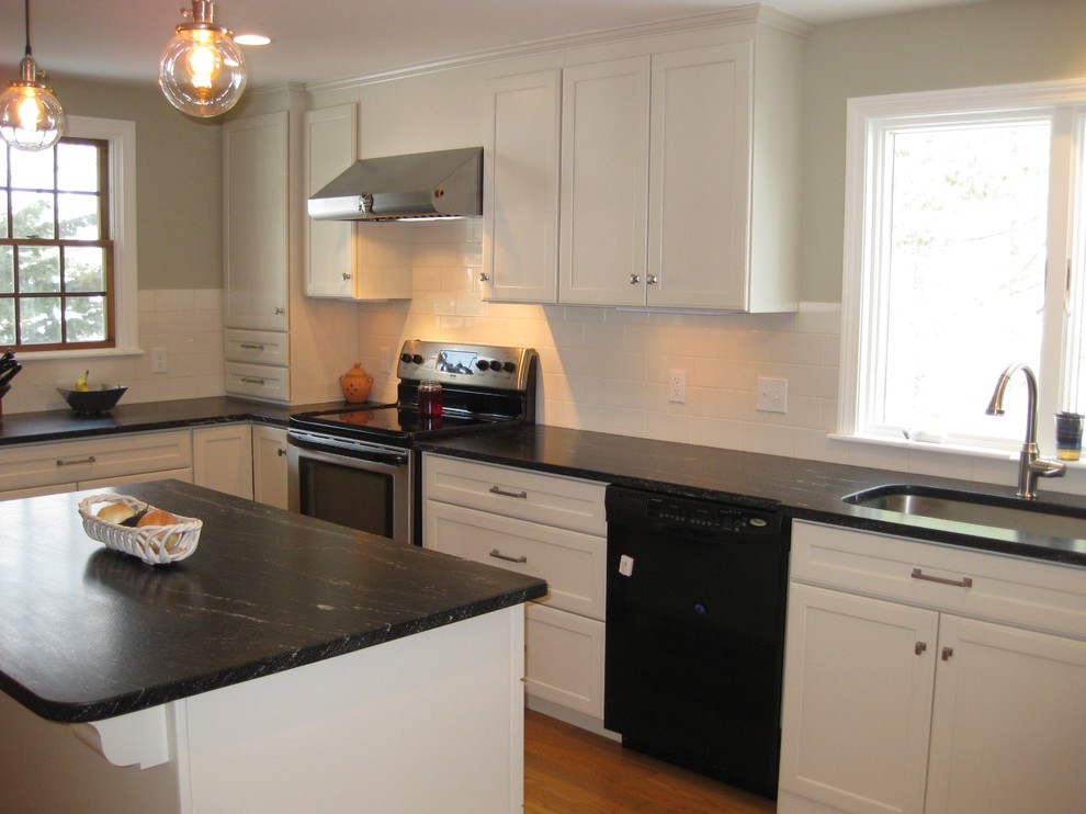 Example of a transitional l-shaped medium tone wood floor eat-in kitchen design in Boston with an undermount sink, shaker cabinets, white cabinets, quartz countertops, white backsplash, ceramic backsplash, stainless steel appliances, an island and black countertops