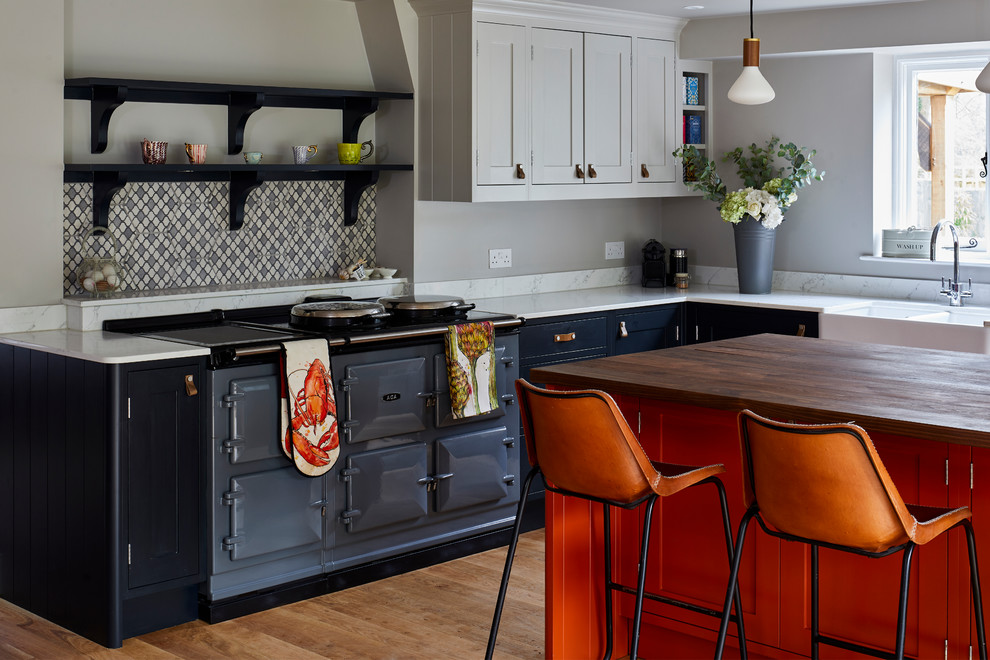 Inspiration for a transitional l-shaped kitchen in Dorset with a farmhouse sink, shaker cabinets, blue cabinets, coloured appliances, medium hardwood floors, with island, brown floor and white benchtop.
