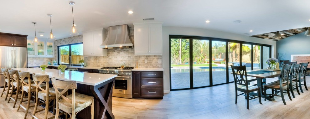 Example of a mid-sized transitional l-shaped light wood floor open concept kitchen design in Phoenix with an undermount sink, shaker cabinets, dark wood cabinets, solid surface countertops, beige backsplash, stone tile backsplash, stainless steel appliances and an island