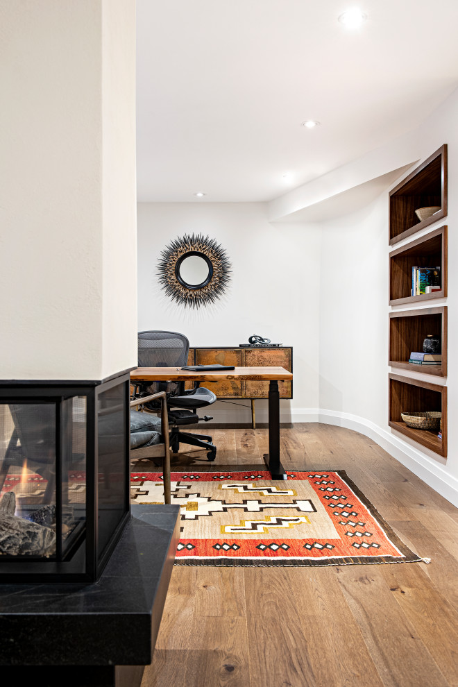 This is an example of a medium sized contemporary home office in Toronto with medium hardwood flooring, a two-sided fireplace, a plastered fireplace surround and a freestanding desk.