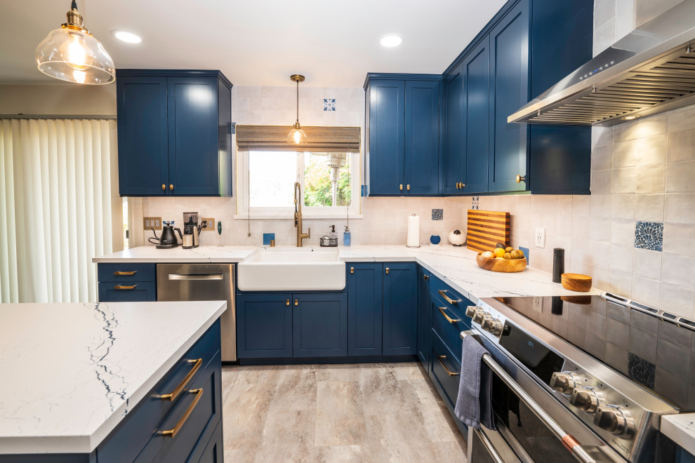 Photo of a large eclectic u-shaped kitchen/diner in San Luis Obispo with a belfast sink, shaker cabinets, blue cabinets, engineered stone countertops, white splashback, ceramic splashback, stainless steel appliances, porcelain flooring, an island, beige floors and white worktops.