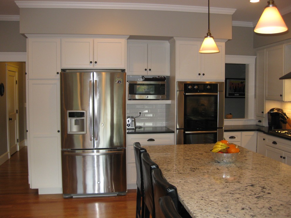 Example of a transitional l-shaped medium tone wood floor eat-in kitchen design in Boston with an undermount sink, shaker cabinets, white cabinets, granite countertops, white backsplash, ceramic backsplash, stainless steel appliances, an island and black countertops