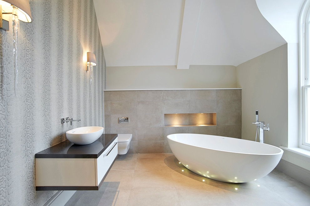 This is an example of a mid-sized contemporary master bathroom in London with a freestanding tub, a wall-mount toilet, flat-panel cabinets, white cabinets, brown tile, a vessel sink and black benchtops.