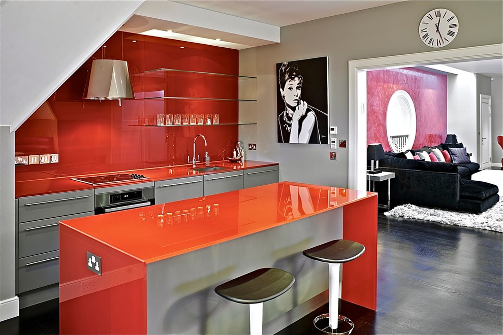Photo of a contemporary single-wall kitchen in London with an undermount sink, flat-panel cabinets, grey cabinets, red splashback, glass sheet splashback and stainless steel appliances.