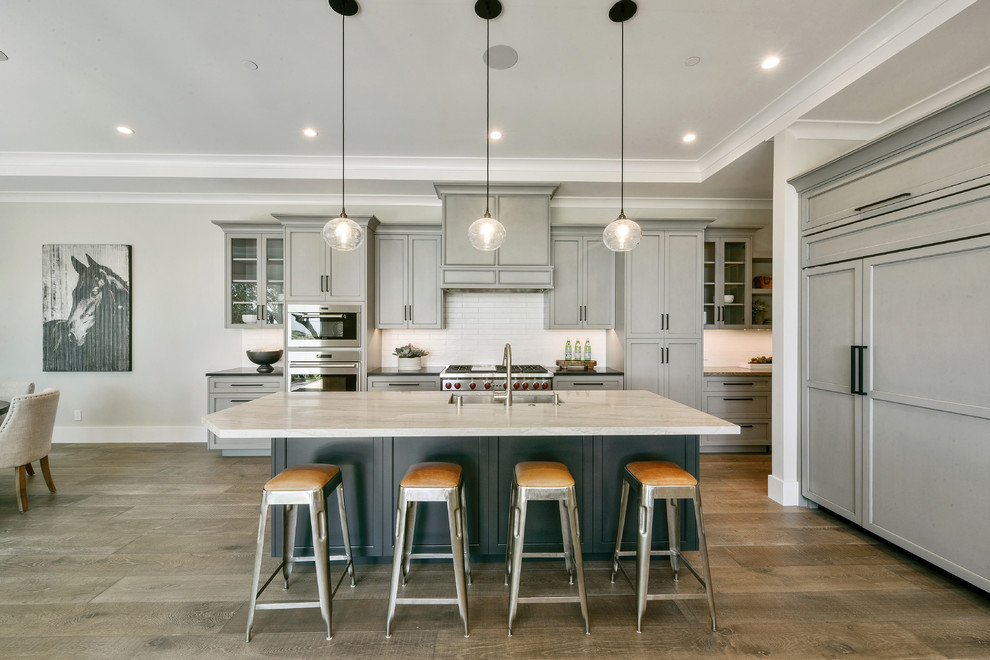 This is an example of a transitional l-shaped eat-in kitchen in San Francisco with an undermount sink, shaker cabinets, grey cabinets, white splashback, panelled appliances, medium hardwood floors, with island, brown floor and white benchtop.