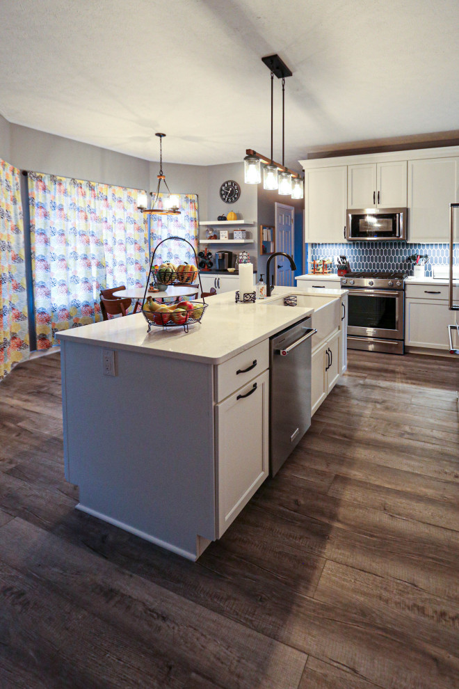 This is an example of a mid-sized transitional l-shaped eat-in kitchen in Cleveland with a farmhouse sink, flat-panel cabinets, white cabinets, quartz benchtops, blue splashback, ceramic splashback, stainless steel appliances, medium hardwood floors, with island, brown floor and white benchtop.