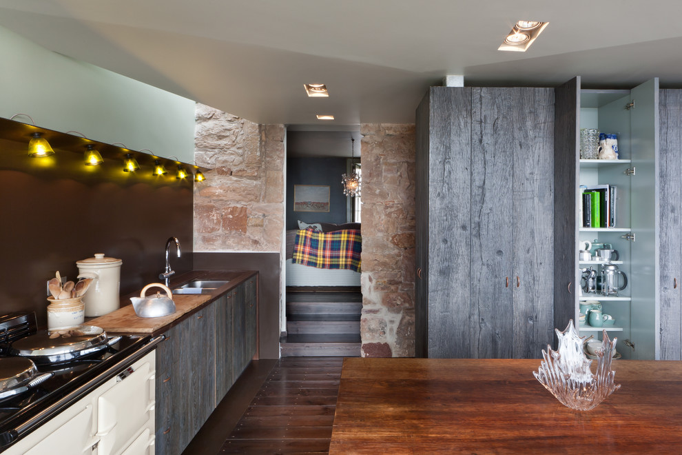 Design ideas for a mid-sized country single-wall eat-in kitchen in London with a double-bowl sink, dark hardwood floors, with island, brown floor, flat-panel cabinets, grey cabinets, wood benchtops, brown splashback and brown benchtop.