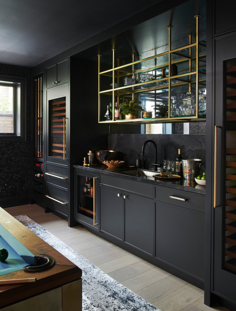 This is an example of a large classic single-wall wet bar in Toronto with a submerged sink, black cabinets, black splashback, light hardwood flooring, black worktops, shaker cabinets and beige floors.
