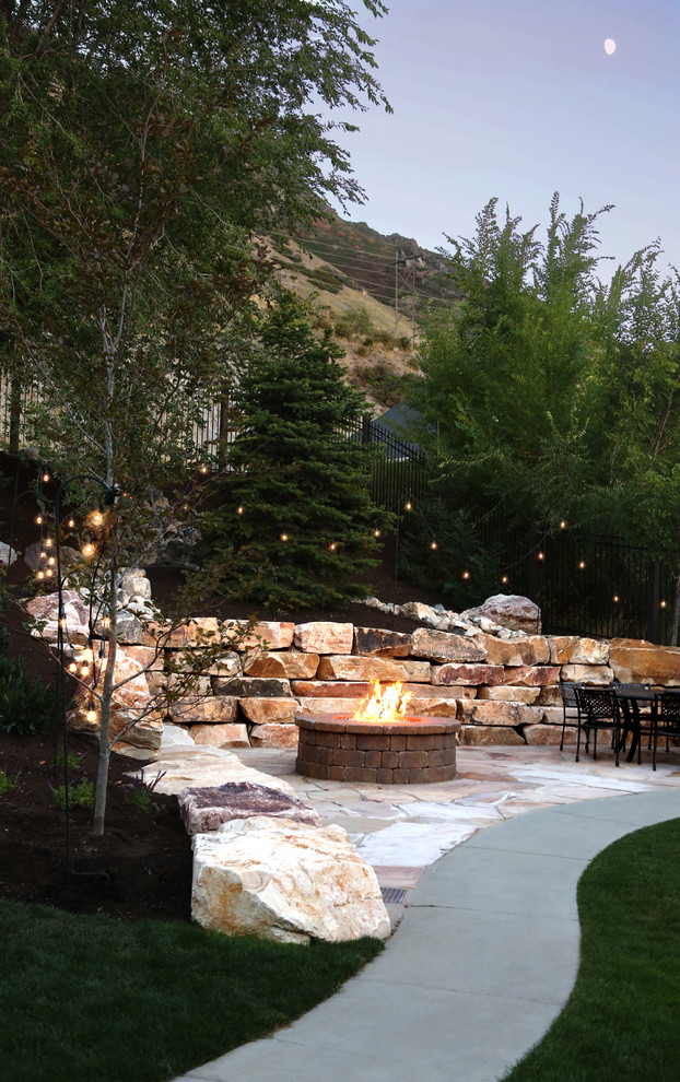 Photo of a large traditional backyard garden in Salt Lake City with a fire feature, natural stone pavers and a metal fence.