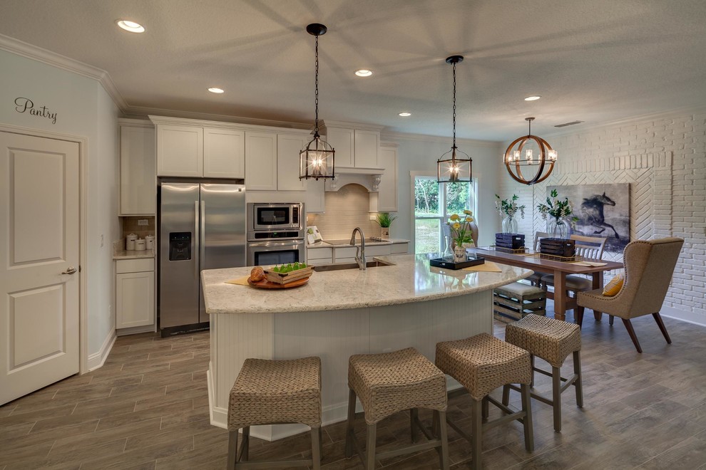 This is an example of a mid-sized transitional l-shaped eat-in kitchen in Jacksonville with a farmhouse sink, shaker cabinets, white cabinets, granite benchtops, beige splashback, subway tile splashback, stainless steel appliances, laminate floors and with island.