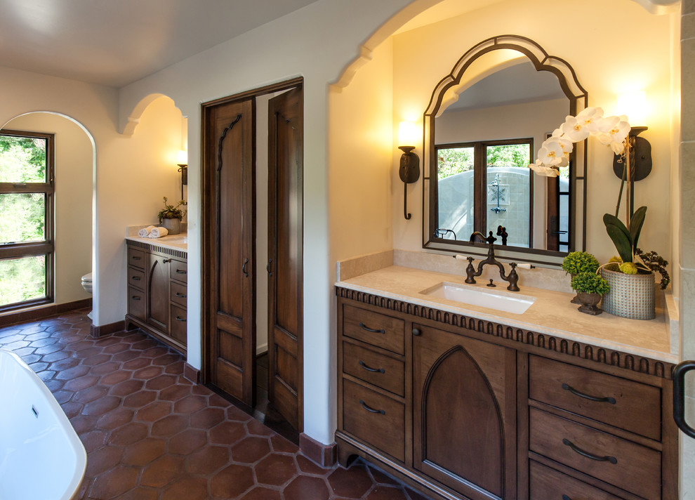 Design ideas for a large mediterranean master bathroom in Santa Barbara with an undermount sink, recessed-panel cabinets, dark wood cabinets, limestone benchtops, a freestanding tub, an open shower, a two-piece toilet, beige tile, terra-cotta tile, white walls and terra-cotta floors.
